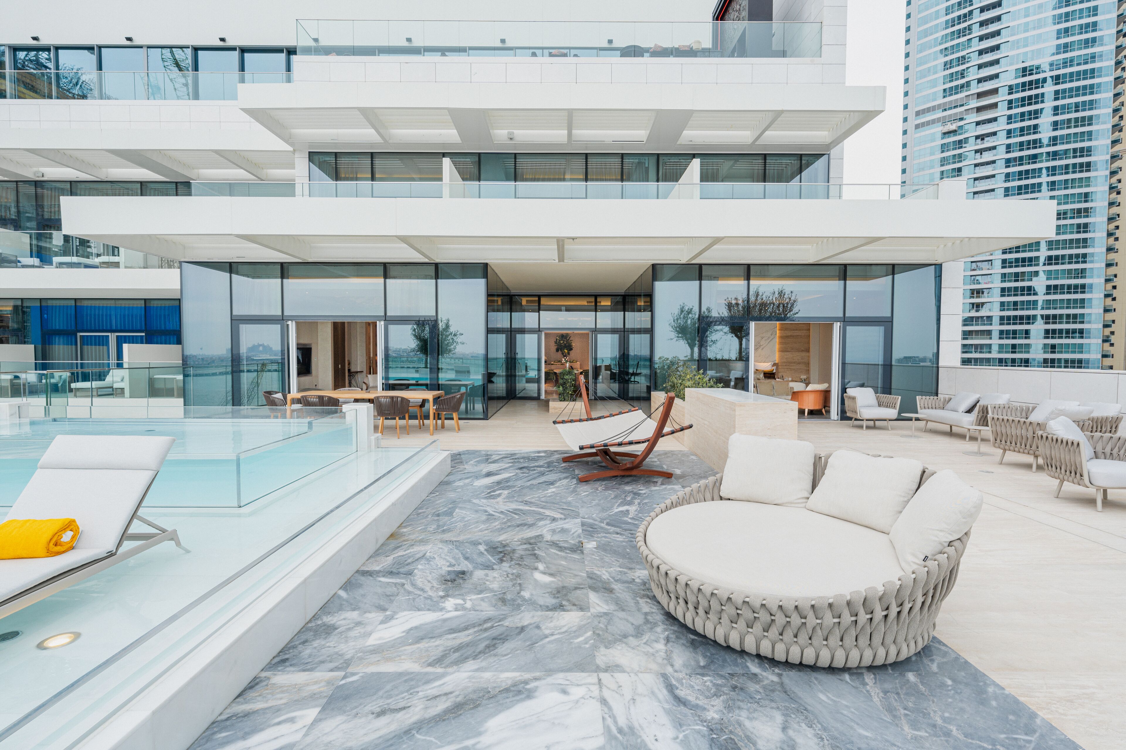 A modern outdoor lounge area with a pool, seating, and a view of the city.