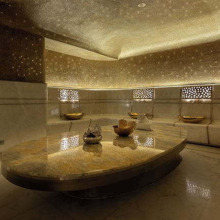 A luxurious spa area with a marble floor, a central round table, and seating with decorative bowls.