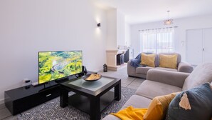 A modern living room with a flat-screen TV, a black coffee table, a beige sofa, and a patterned rug. - Vila da Pesca House (Rabo de Peixe)