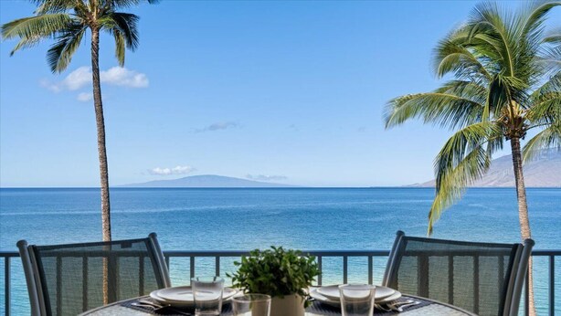 A table set for dining with a view of the ocean and palm trees. - Oceanfront Kihei condo w/ sunset views and pool (Kihei)