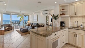 A modern kitchen with a large island, built-in cabinets, and a view to the outside. - Oceanfront Kihei condo w/ sunset views and pool (Kihei)