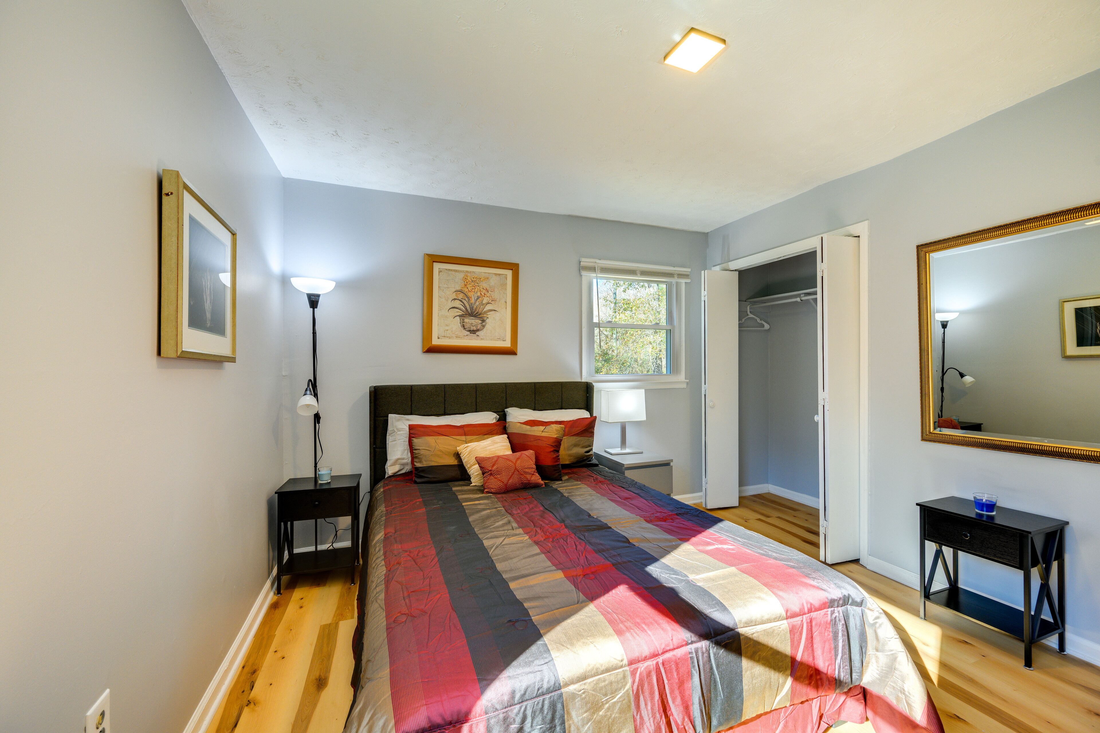 Une chambre à coucher comprenant un lit, des tables de chevet, une commode, une fenêtre, un placard et un miroir.