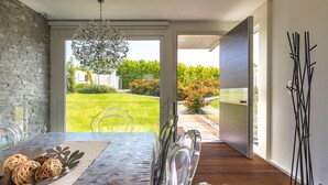 Un interno moderno con zona pranzo, vista su un giardino e una porta scorrevole che dà sull'esterno.