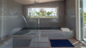 Un bagno moderno con doccia vetrata, vasca da bagno con vista sull'esterno e tappetino blu sul pavimento.