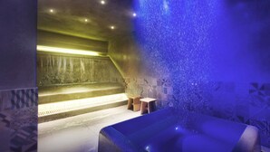 Une salle de spa avec un élément décoratif aquatique illuminé de lumière bleue, une table de massage et un petit tabouret en bois.