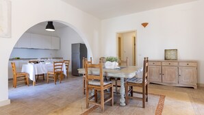 A dining area with a table set for two, wooden chairs, a refrigerator, and a cabinet. - Villa Floria 4, Emma Villas (Gagliano del Capo)