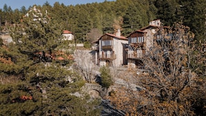 A stone building with multiple balconies and a red-tiled roof, surrounded by trees and a mountainous backdrop. - Parnassus Woodstone Chalets- N1- N2- N3 (Delphi)