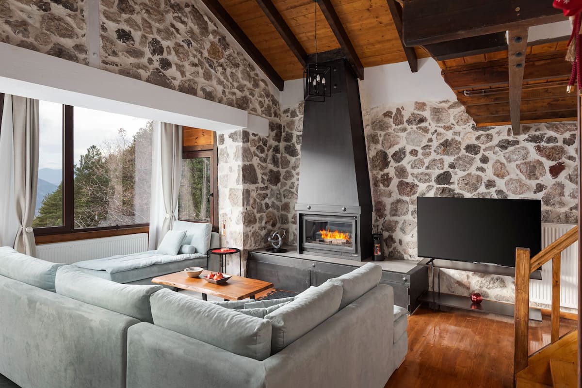 Ein gemütliches Wohnzimmer mit Steinwand, Kamin, Sofa und Fernseher.