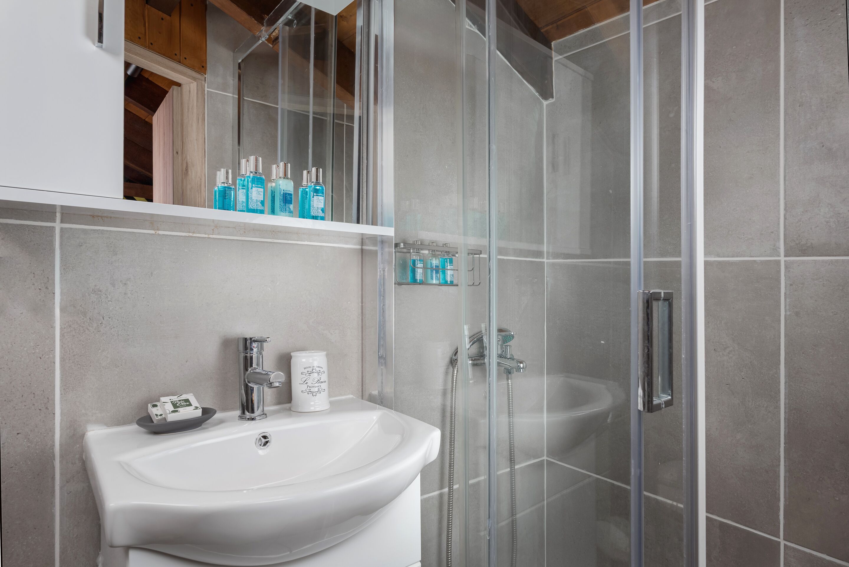 A modern bathroom with a white sink, glass shower enclosure, and a shelf with toiletries.
