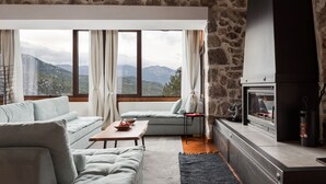 A living room with a stone wall, a fireplace, a sofa, a coffee table, and a view of mountains. - Parnassus Woodstone Chalets- N1- N2- N3 (Delphi)