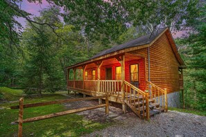 A wooden cabin with a porch, surrounded by trees.