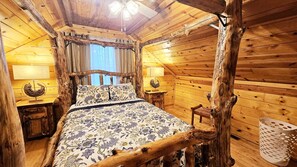 Um quarto rústico de madeira com uma cama, duas mesas de cabeceira, um abajur e uma janela com cortinas.