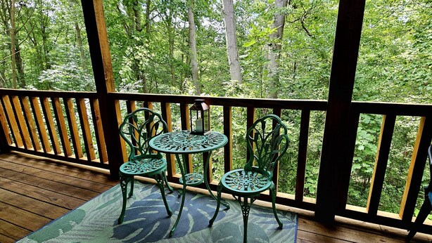 A wooden deck with a railing, two green metal chairs, and a small table. - Green Heron in Hocking Hills (Logan)