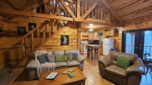 A cozy cabin interior with a wooden staircase, a kitchen area, and two leather sofas with cushions. - Green Heron in Hocking Hills (Logan)