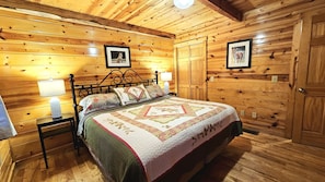A wooden cabin bedroom with a bed, nightstands, and framed pictures on the walls. - Green Heron in Hocking Hills (Logan)