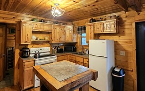 A wooden cabin kitchen with a stove, microwave, sink, and refrigerator.
