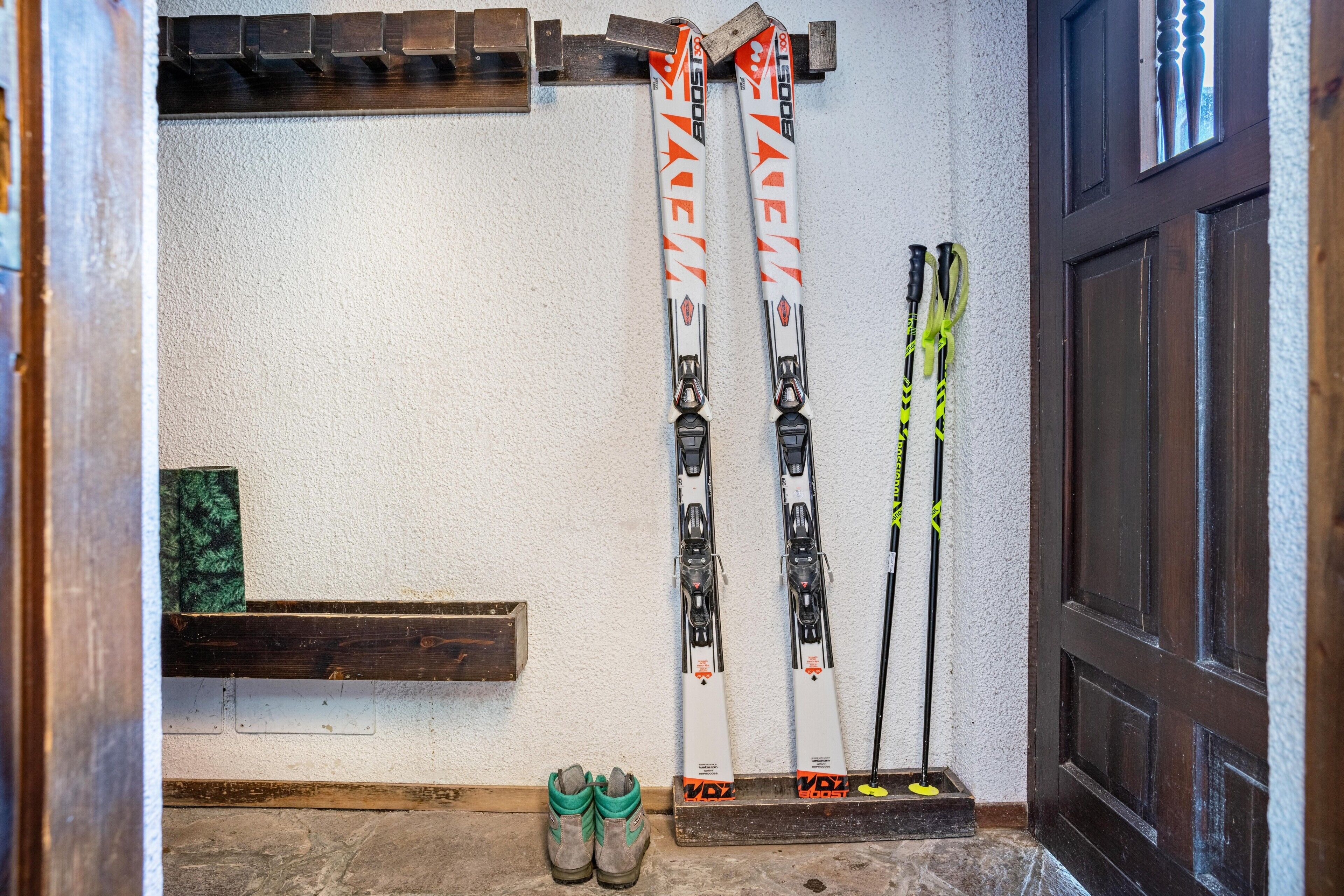 A ski rack with skis and poles, a pair of boots, and a wooden shelf.