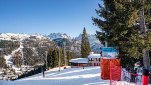 A snow-covered ski slope with a sign indicating a mountain peak and a building with a red roof.