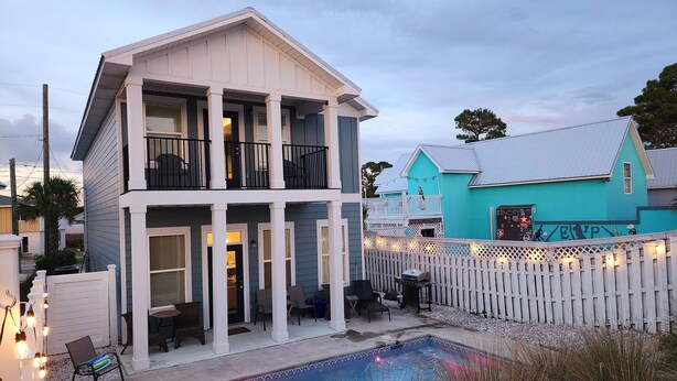 Una casa de dos pisos con balcón, piscina y cerca blanca en forma de piquete.