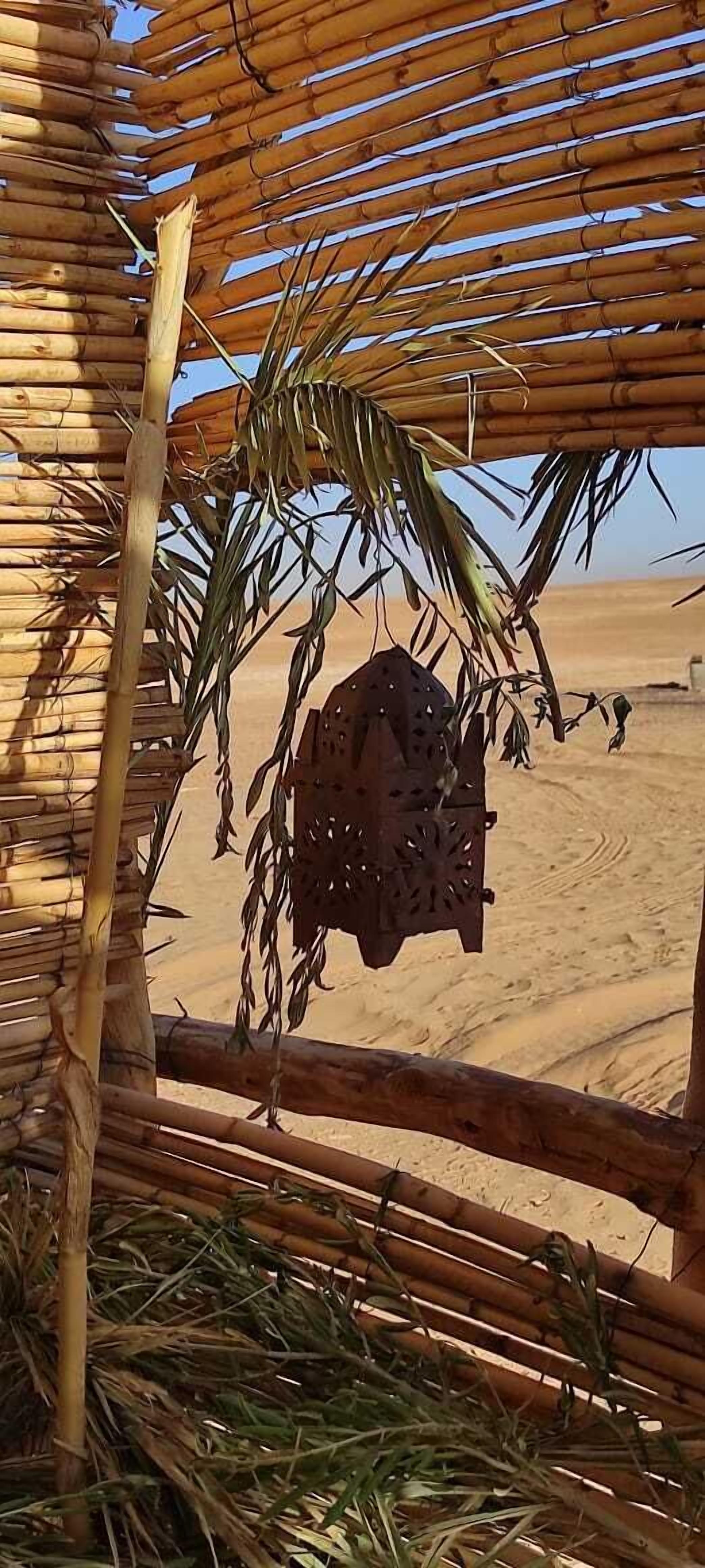 Une structure en bambou ornée d’un élément décoratif suspendu, située dans un environnement désertique.