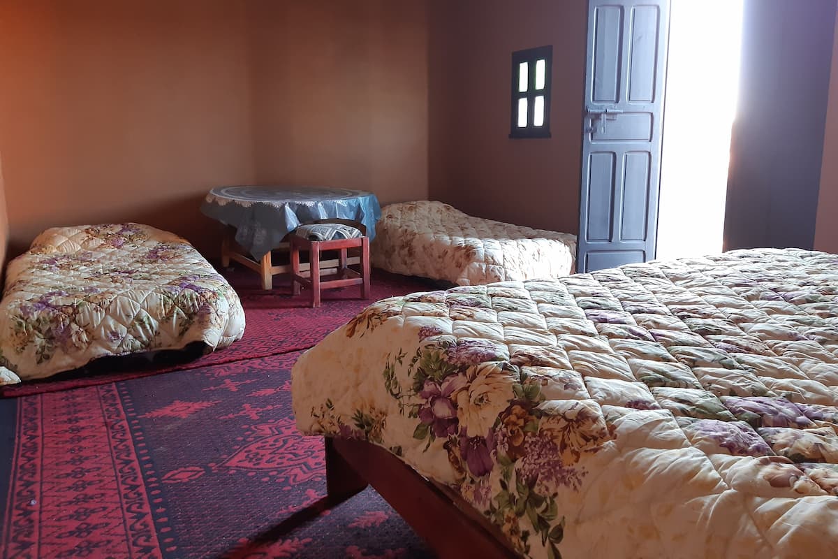Une chambre avec un grand lit, deux petits lits, une table avec une chaise et une porte.