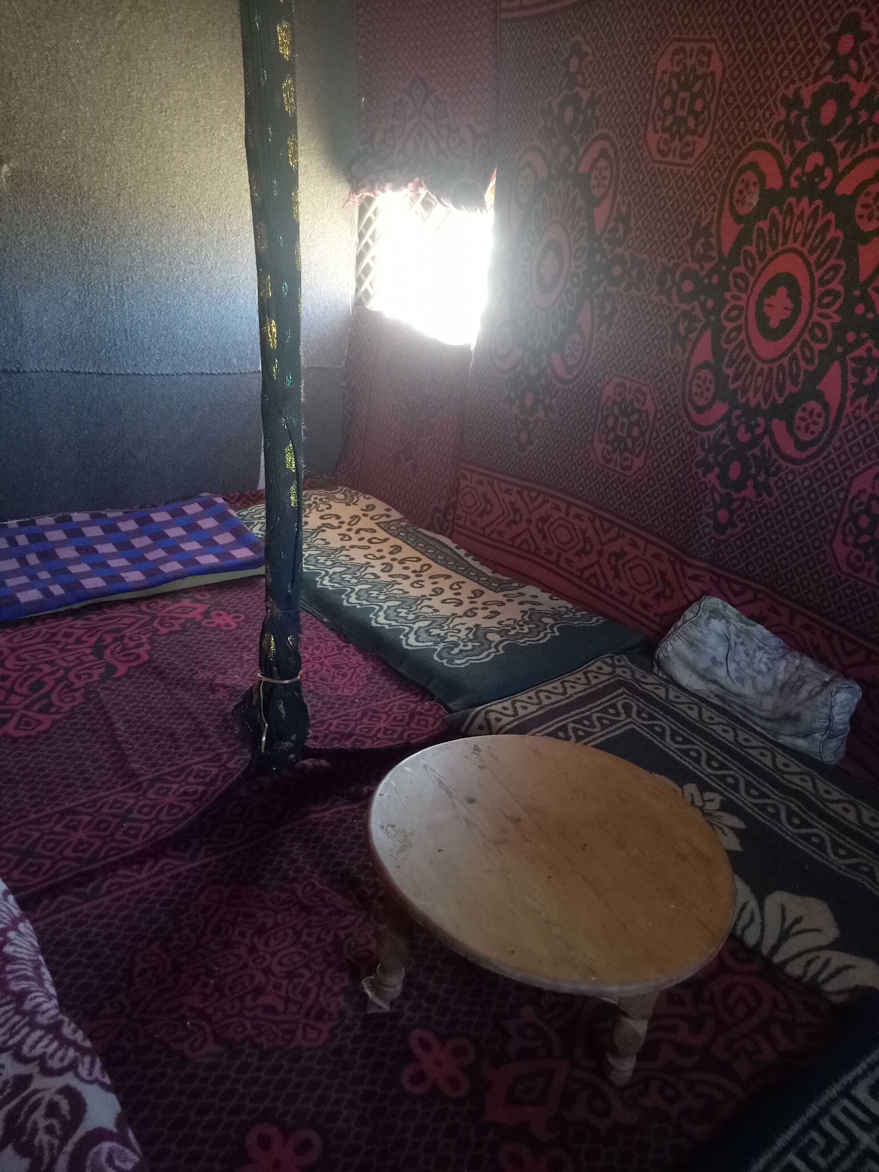 Una habitación con paredes de diseño, suelo de madera, una mesa redonda pequeña y un banco.