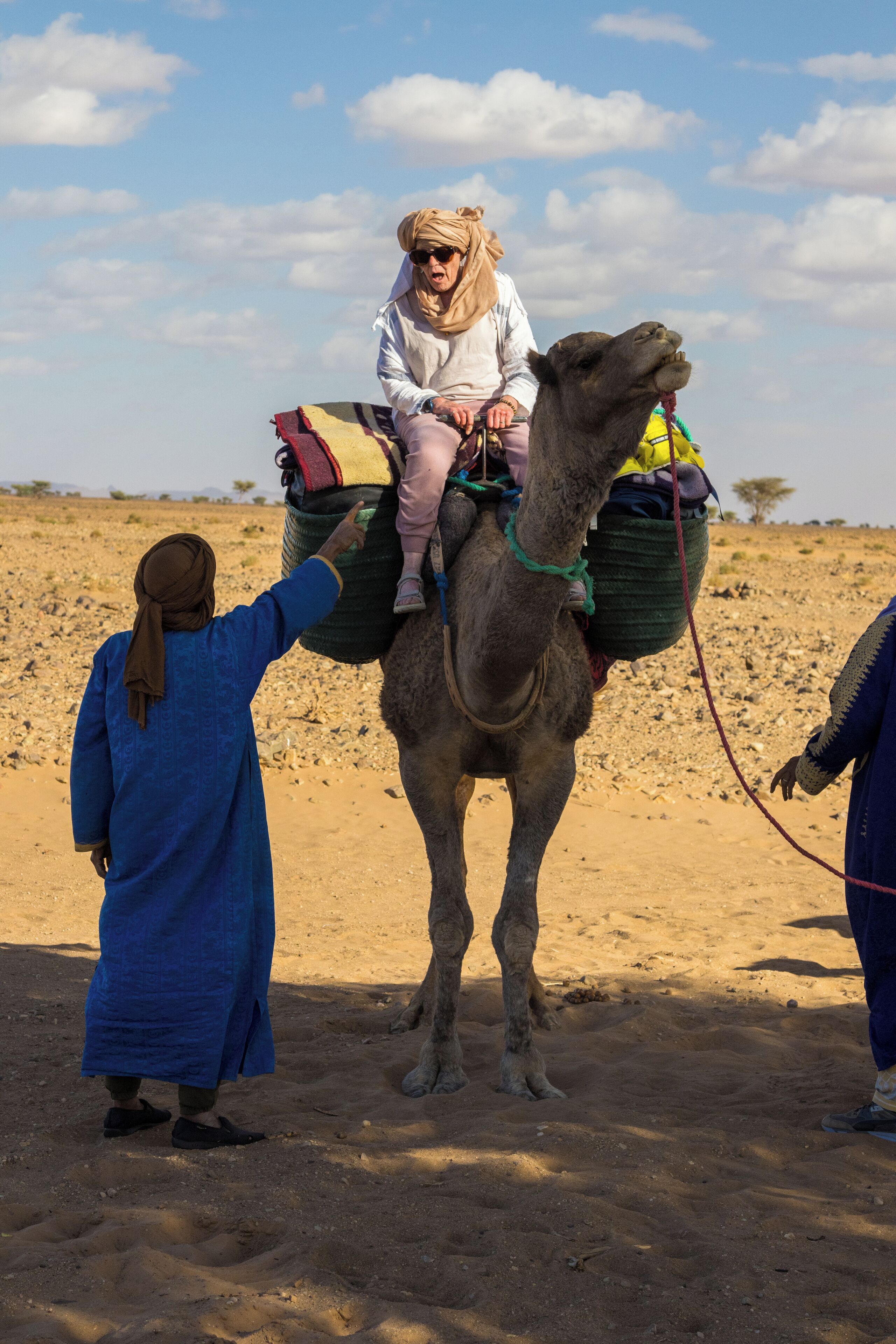 A camel with a child and two people in a desert setting.