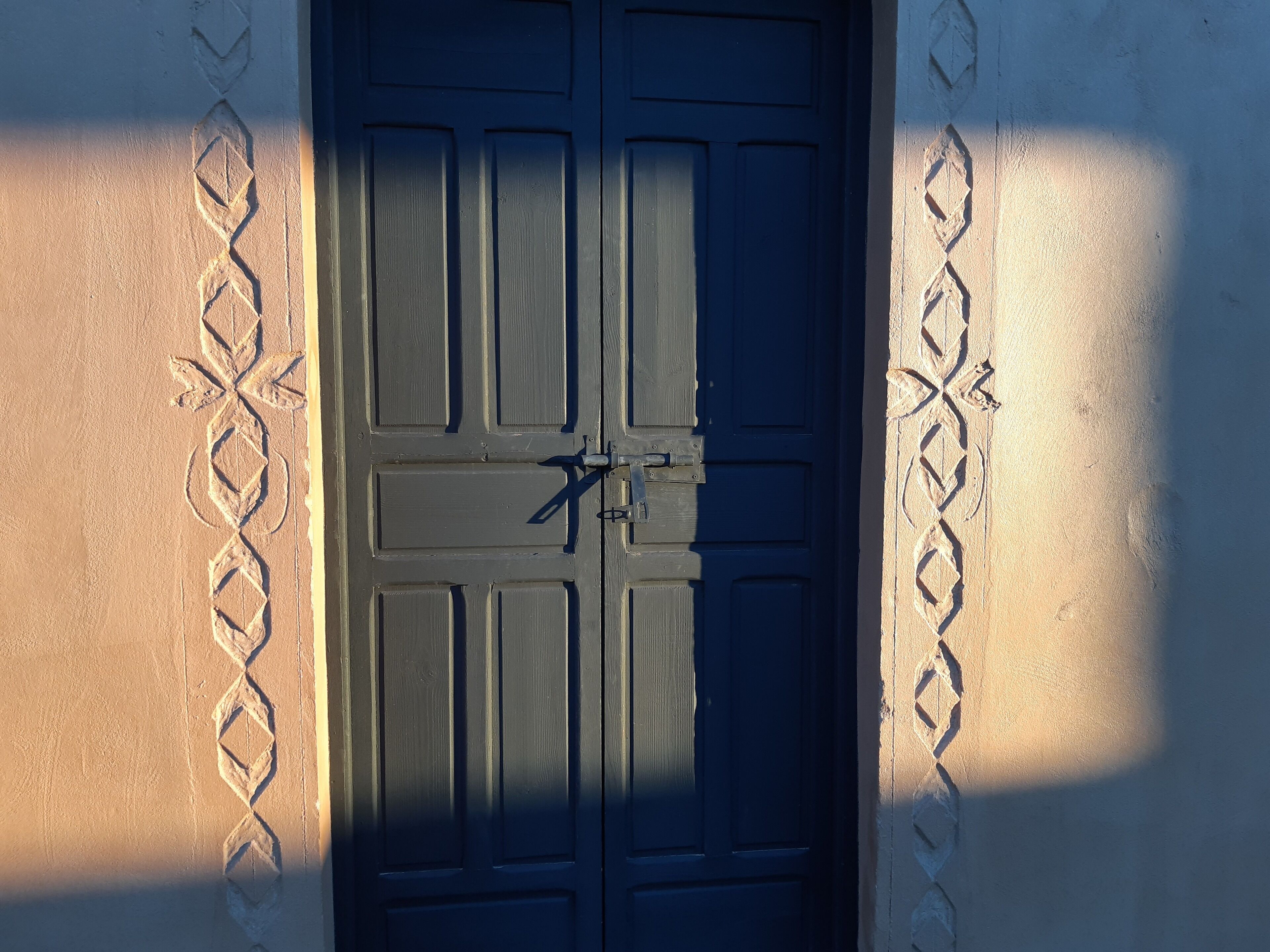 A closed dark wooden door with a metal latch, set in a wall with decorative patterns.