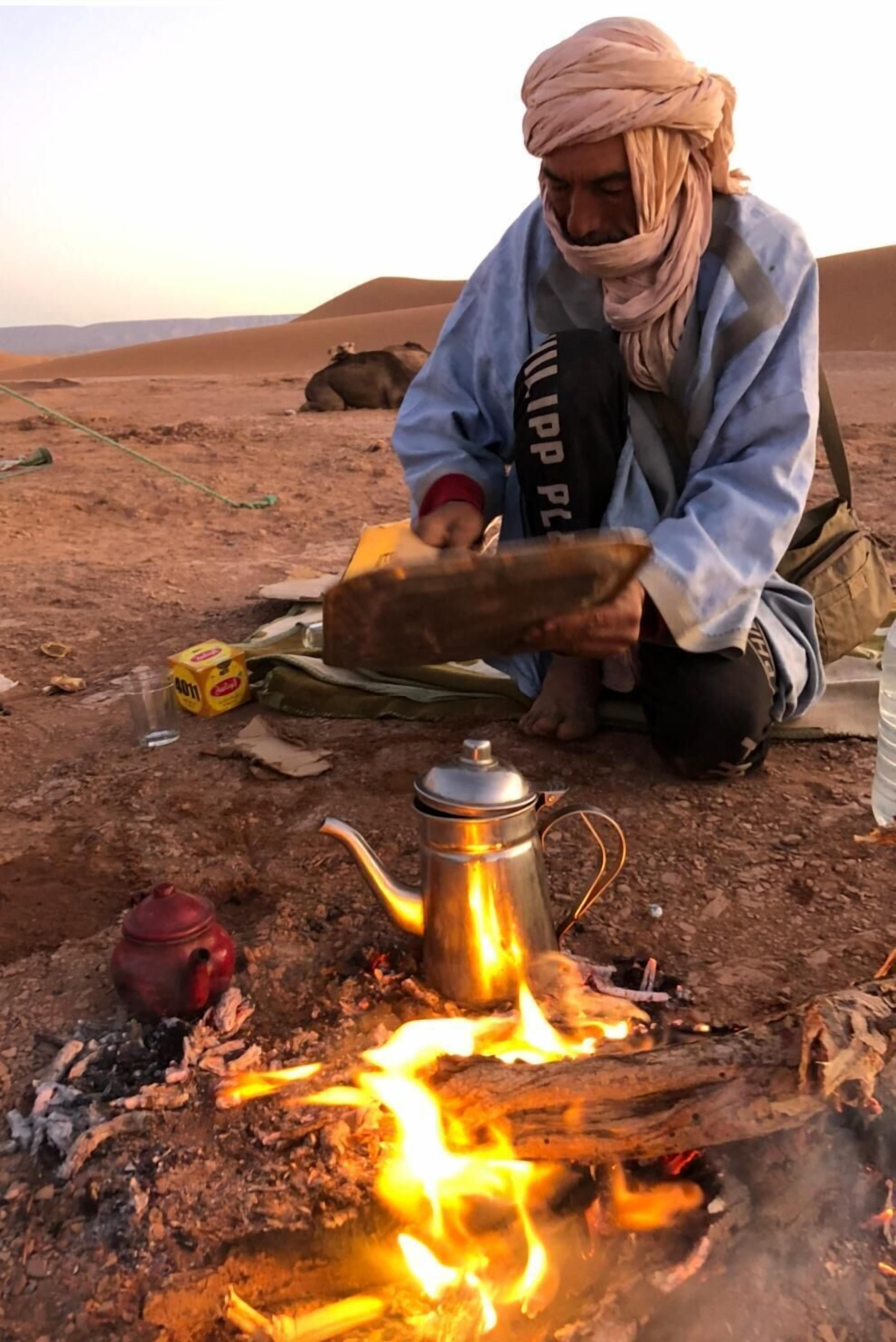 A person cooking over an open fire in a desert setting.