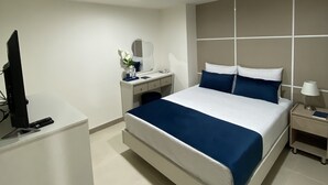 Una habitación de hotel moderna con una cama grande, un escritorio, un televisor y una mesita de noche.