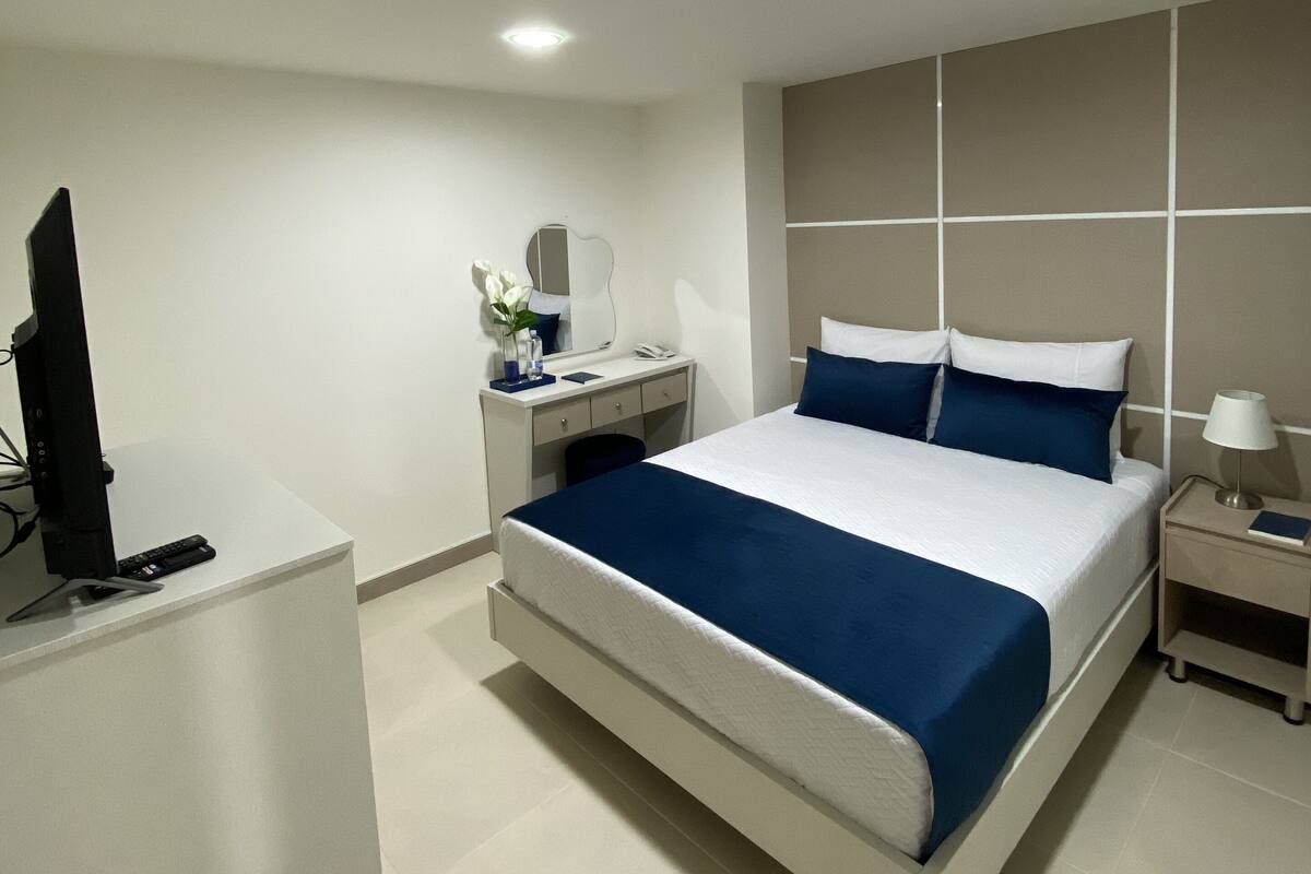 Una habitación de hotel moderna con una cama grande, un escritorio, un televisor y una mesita de noche.