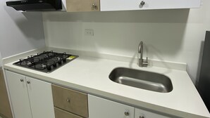 Una cocina con gabinetes blancos, un lavamanos de acero inoxidable y una estufa a gas.