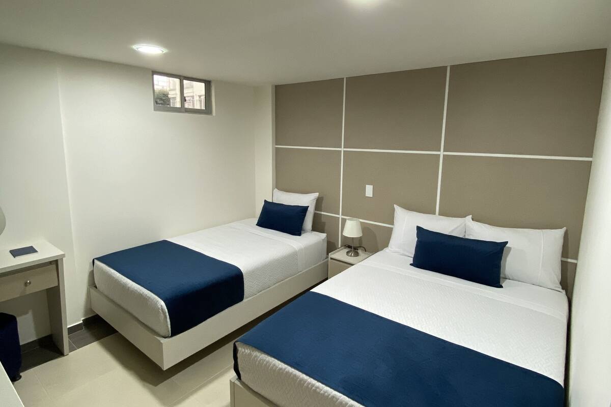 Una habitación de hotel con dos camas, un escritorio, una mesita de noche y una ventana.
