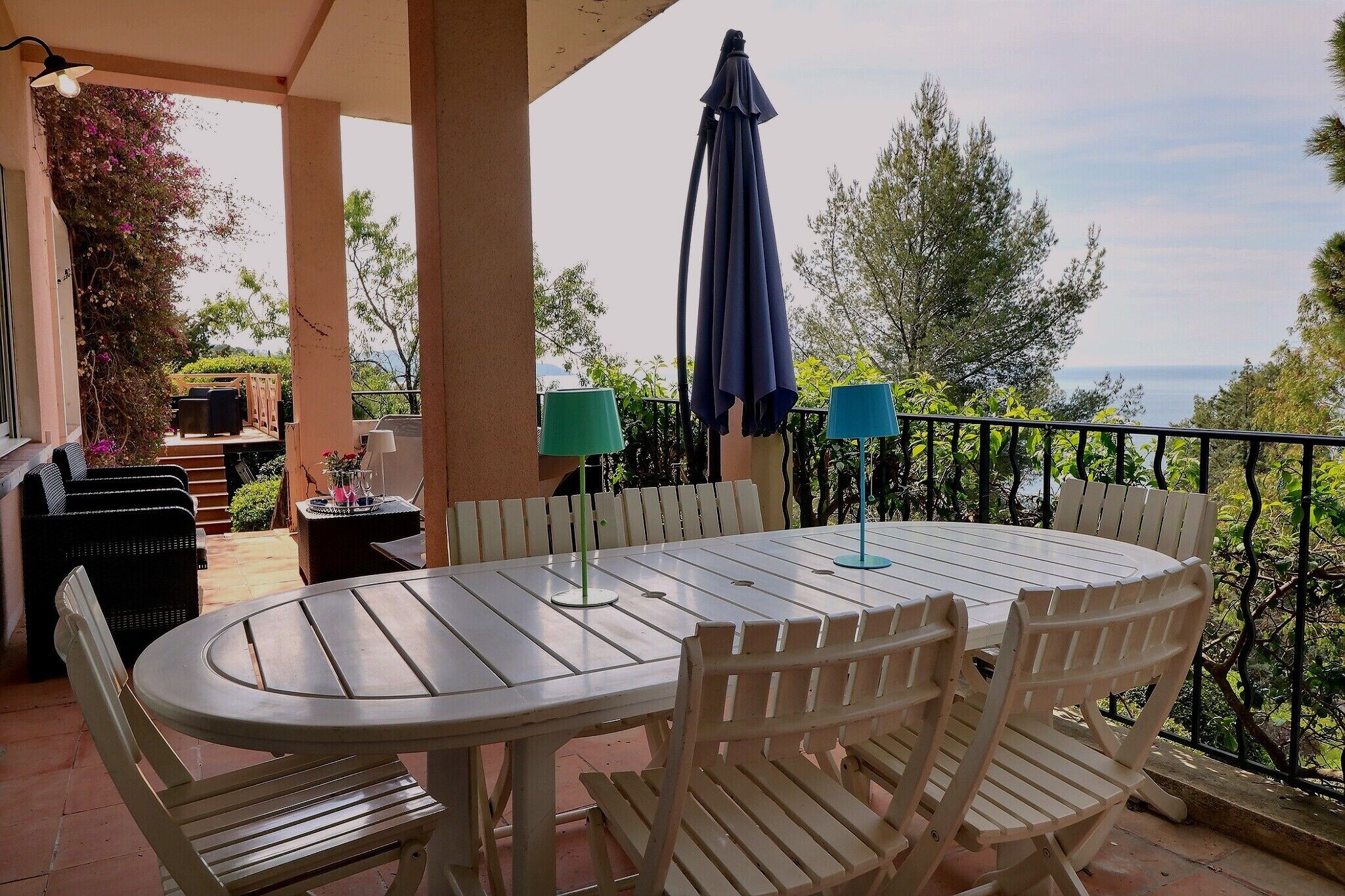 A covered patio with a round table and chairs, a grill, and a view of the sea.