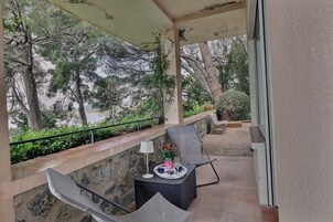 Un área de estar al aire libre techada, con una mesa dispuesta para dos personas, una silla y vistas a árboles y vegetación.