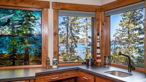 A kitchen with wooden cabinets, a stainless steel sink, and a large window with a view of trees and a dock.