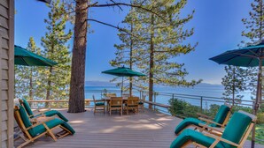 A wooden deck with outdoor furniture, including chairs and a table, overlooking a body of water.