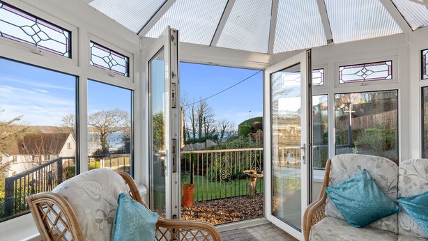 A conservatory with wicker furniture and a view of a garden. - Four Oaks - Sea and Harbour Views (Saundersfoot)