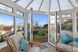 A conservatory with wicker furniture and a view of a garden. - Four Oaks - Sea and Harbour Views (Saundersfoot)