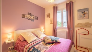 A bedroom with a bed, bedside lamps, a window with curtains, and wall art.