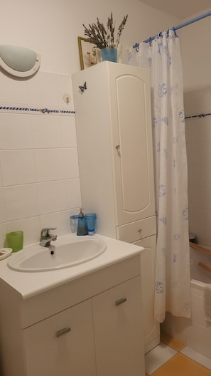 Un baño con lavamanos blanco, espejo, armario y cortina de ducha.