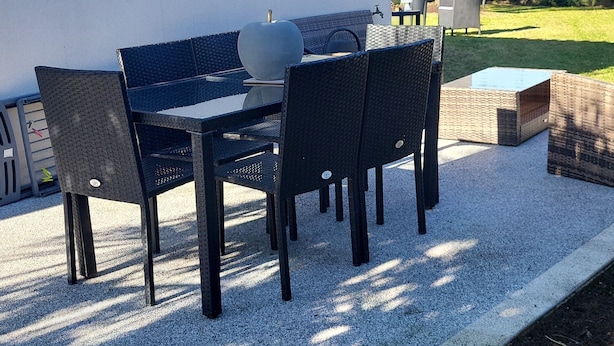 An outdoor patio with a table and chairs, a potted plant, and a tree in the background.