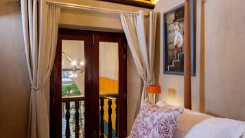 A hotel room with a bed, curtains, a painting, and a view of a balcony.