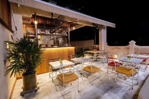 Un espace extérieur aménagé pour les repas, avec des tables et des chaises, un bar et des plantes en pot.