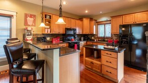 A modern kitchen with wooden cabinets, a black refrigerator, a microwave, and a kettle. - Wolf's Den (Ellicottville)