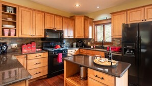 A kitchen with wooden cabinets, a black refrigerator, a stove, and a microwave. - Wolf's Den (Ellicottville)