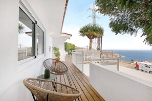 Een balkon met rieten stoelen, een bloempot en uitzicht op zee.