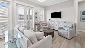 Ein geräumiges Wohnzimmer mit einem Glastisch, einem beigefarbenen Sofa und einem weißen Sessel.