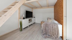 Ein kleines Schlafzimmer mit einem Schlafplatz in der Art eines Lofts, einem weißen TV-Schrank und einer Holztreppe.