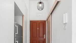 Ein schmaler Korridor mit Holzboden, einer Tür am Ende und einem Kühlschrank links.
